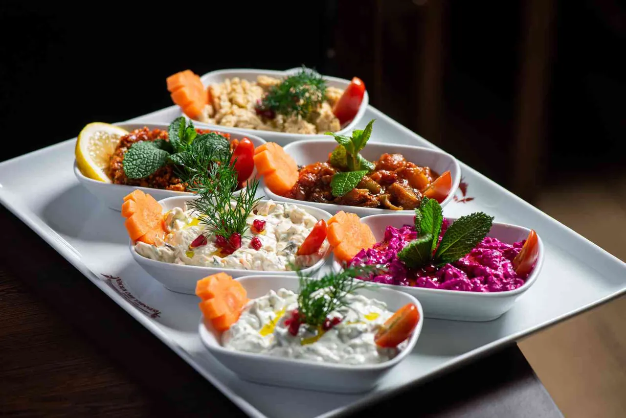 Plated meze selection with hummus, baba ganoush, beetroot dip and other Middle Eastern appetisers, garnished with herbs and carrot.
