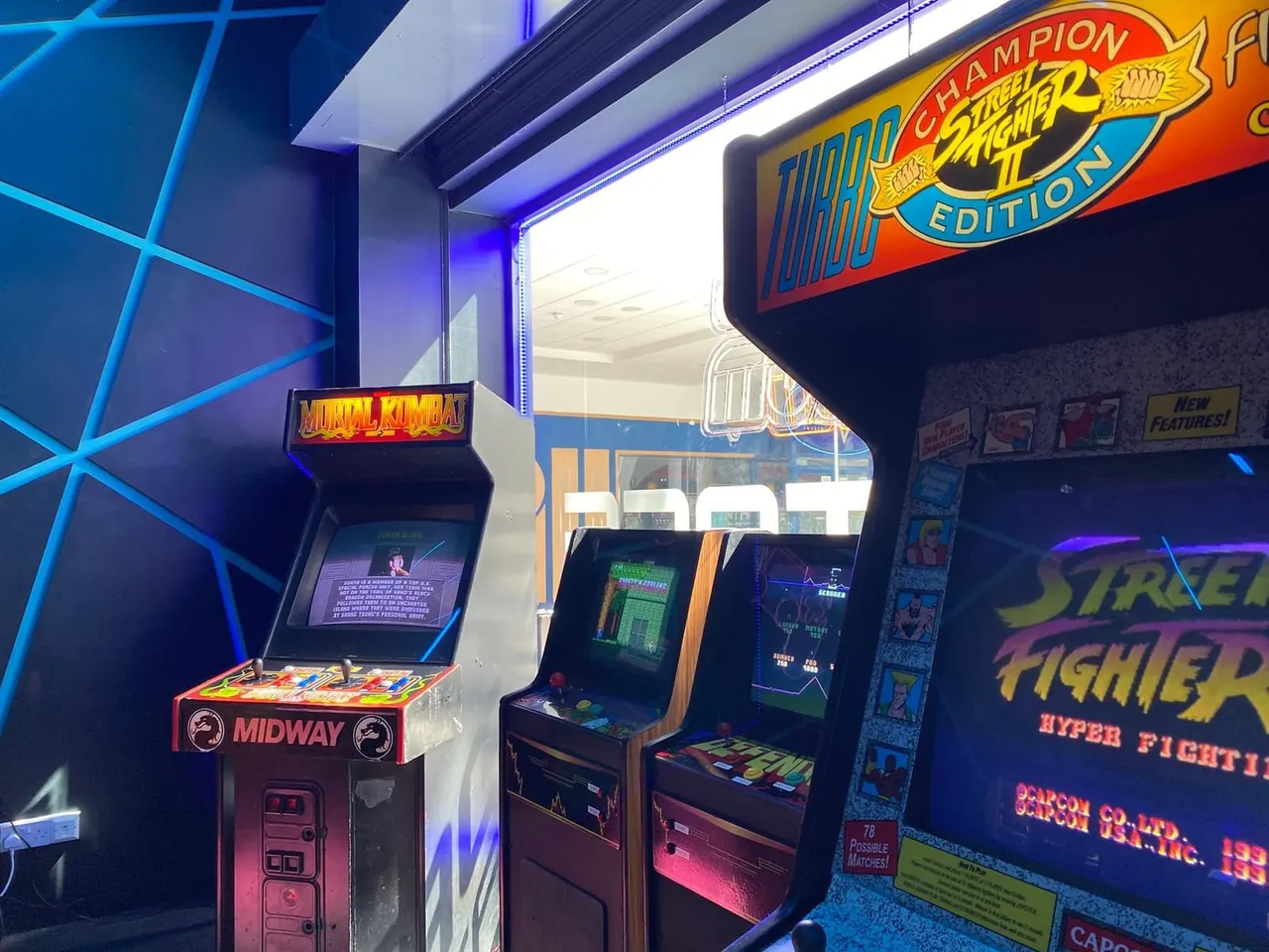 Vintage arcade cabinet games including Mortal Kombat and Street Fighter displayed in neon-lit arcade venue.