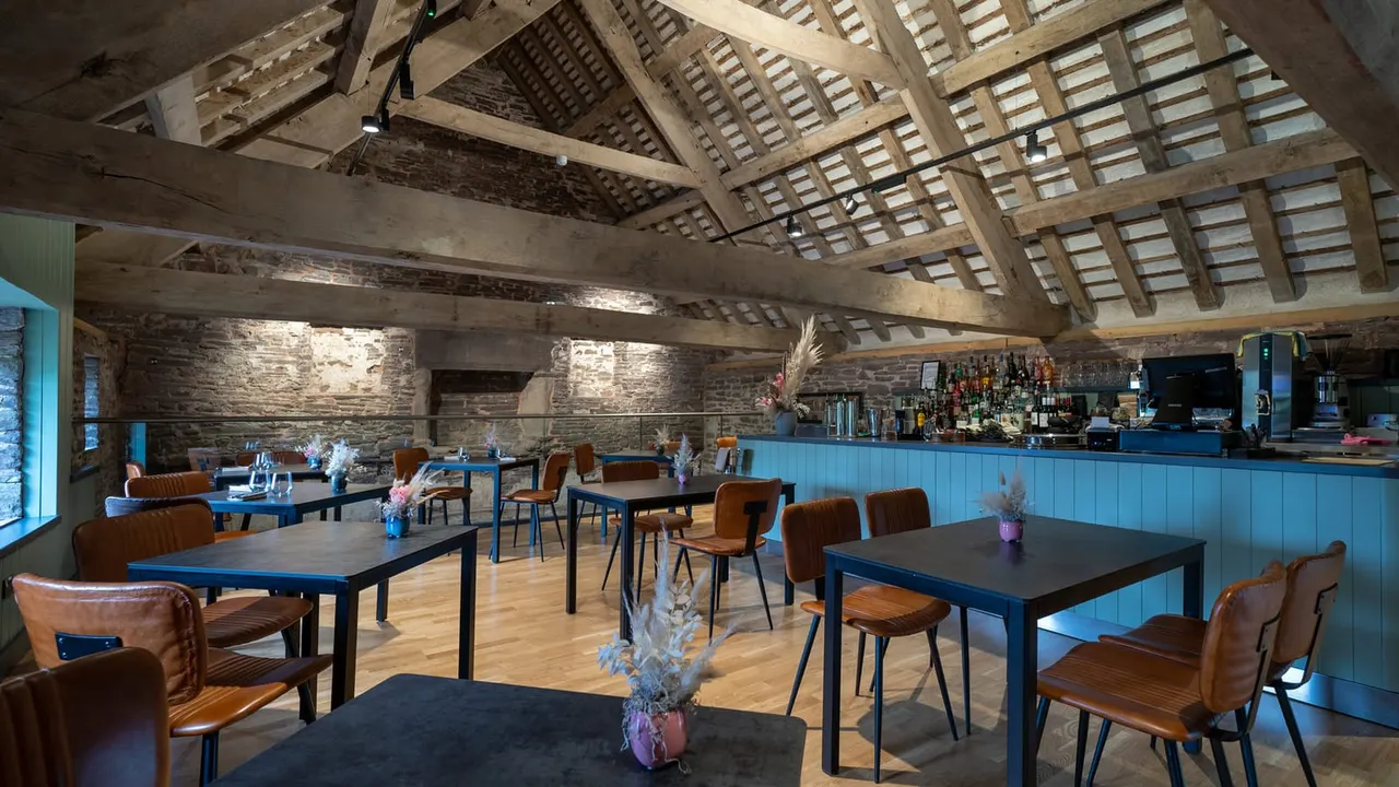 Modern restaurant interior with blue tables, brown chairs, stone walls, exposed wooden beams and bar counter in converted historic building.