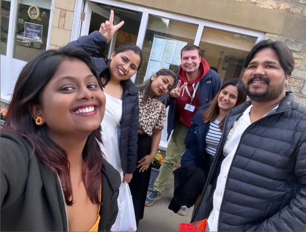 A group of smiling people posing together outside a stone building entrance.