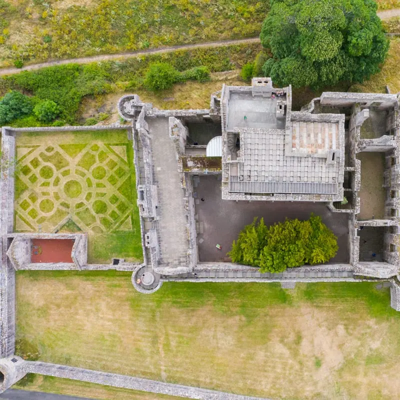 Aerial view of a historic castle courtyard with geometric parterre garden, stone buildings, and surrounding grounds.