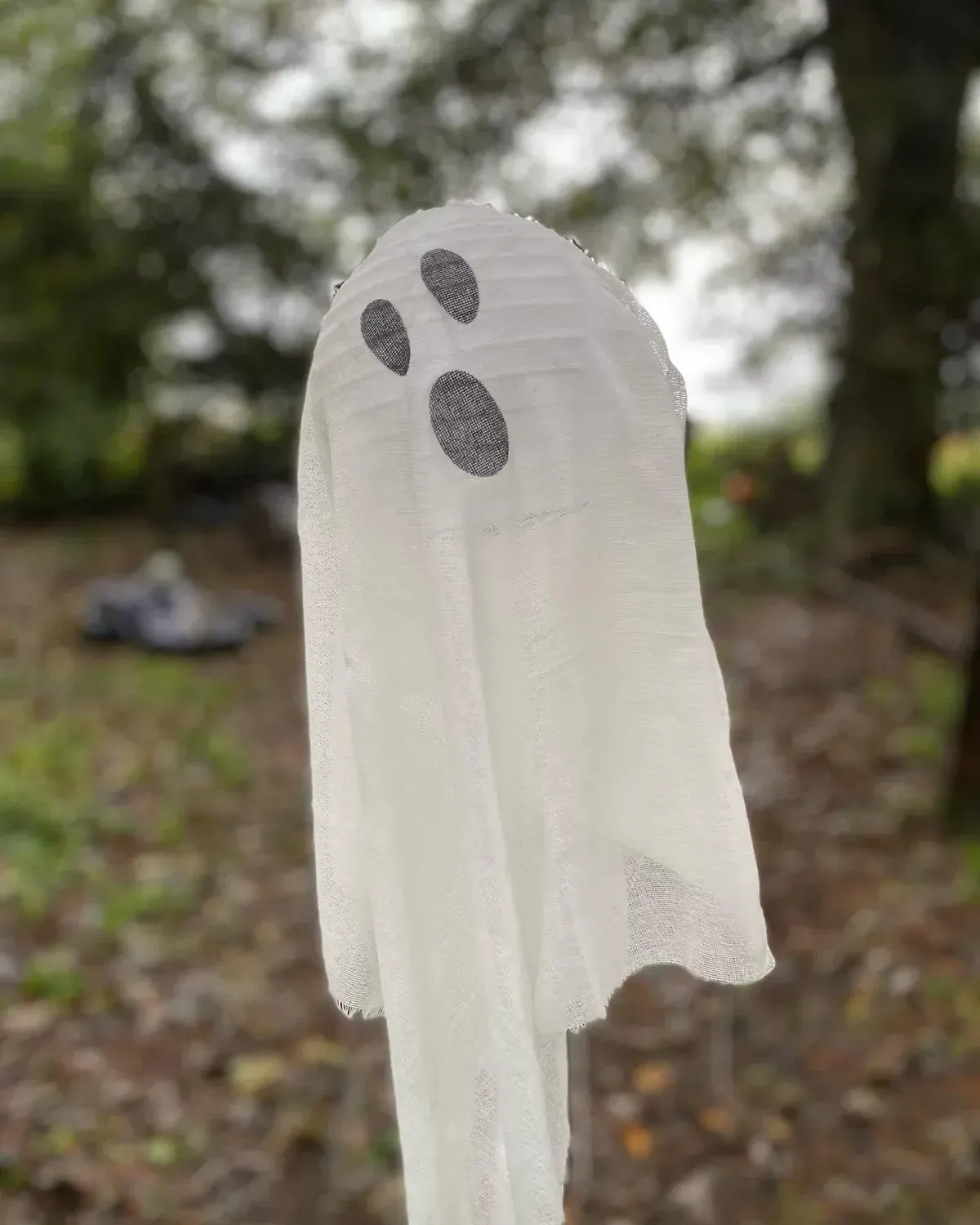 White ghost decoration with dark oval eyes in a garden with flowering trees and shrubs.