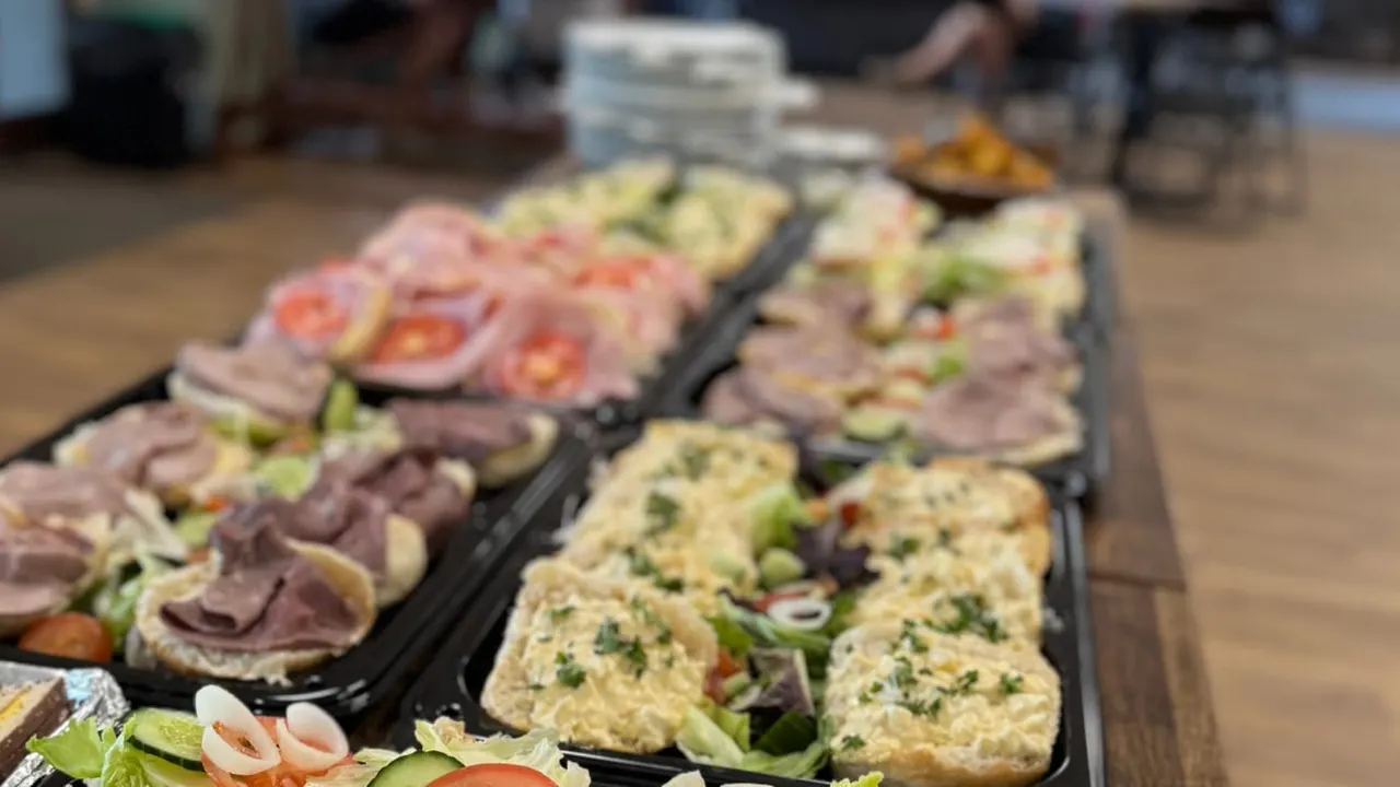 Catered buffet trays of sandwiches and wraps with fresh vegetables and garnishes at an outdoor event.
