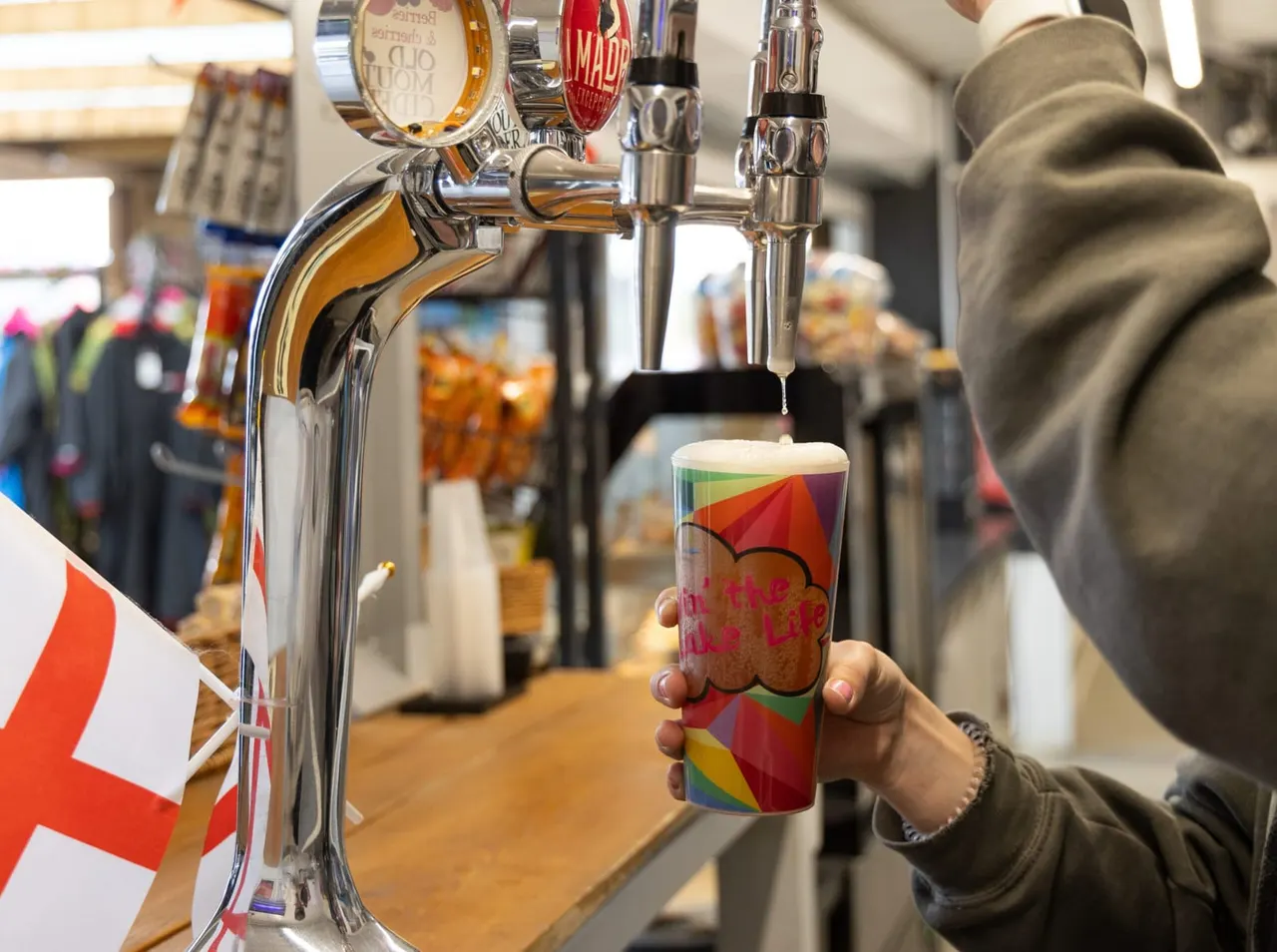 Person pouring beer from a tap into a colourful cup at a bar counter.
