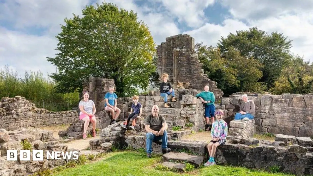 Group of visitors exploring Roman ruins with stone walls and tower structure surrounded by trees and grass.