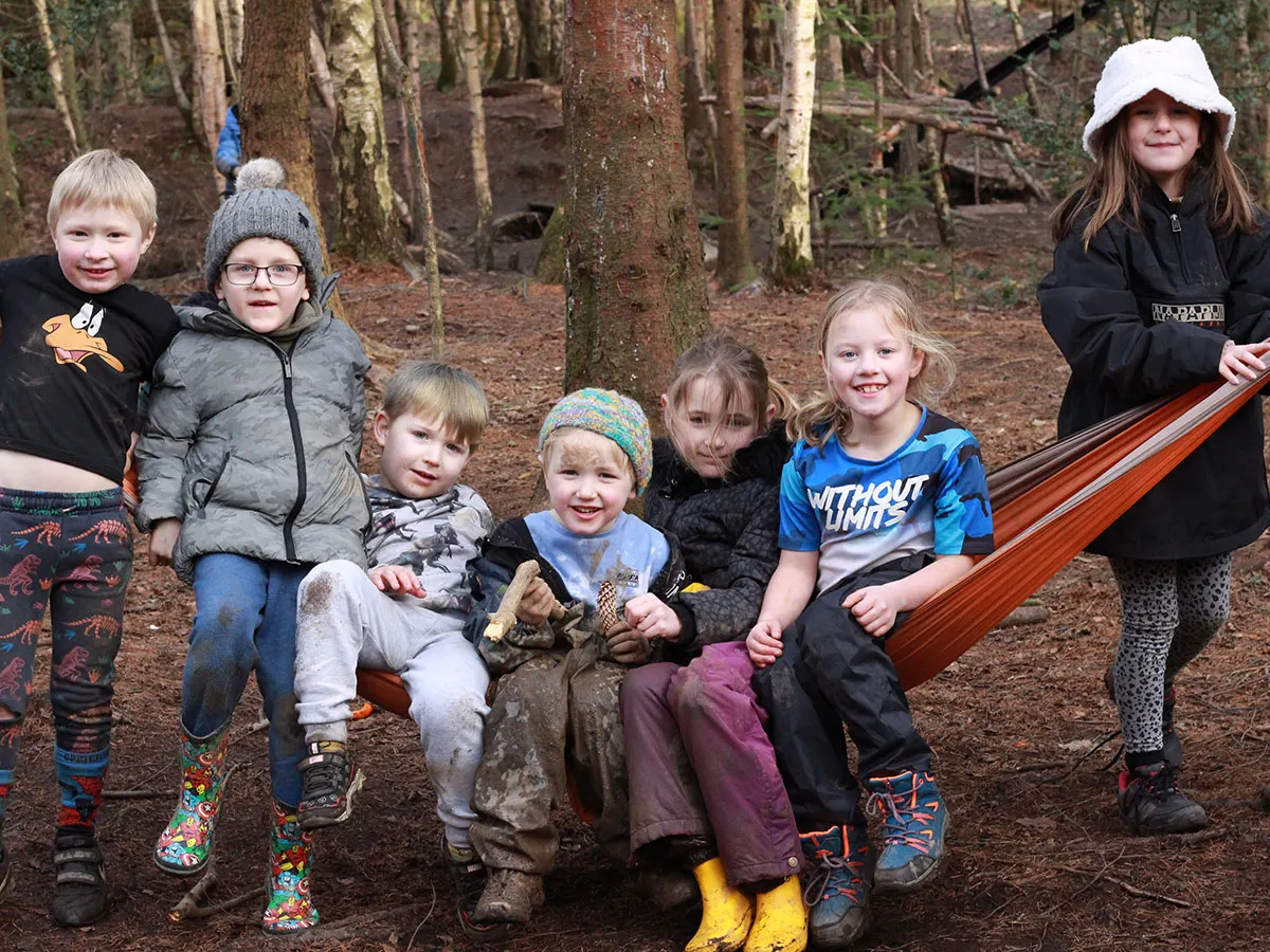 Group of children posing together in a woodland setting with a hammock strung between trees.