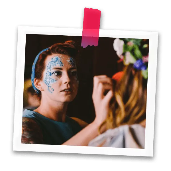 Child having blue face paint applied by an artist during a face painting session.