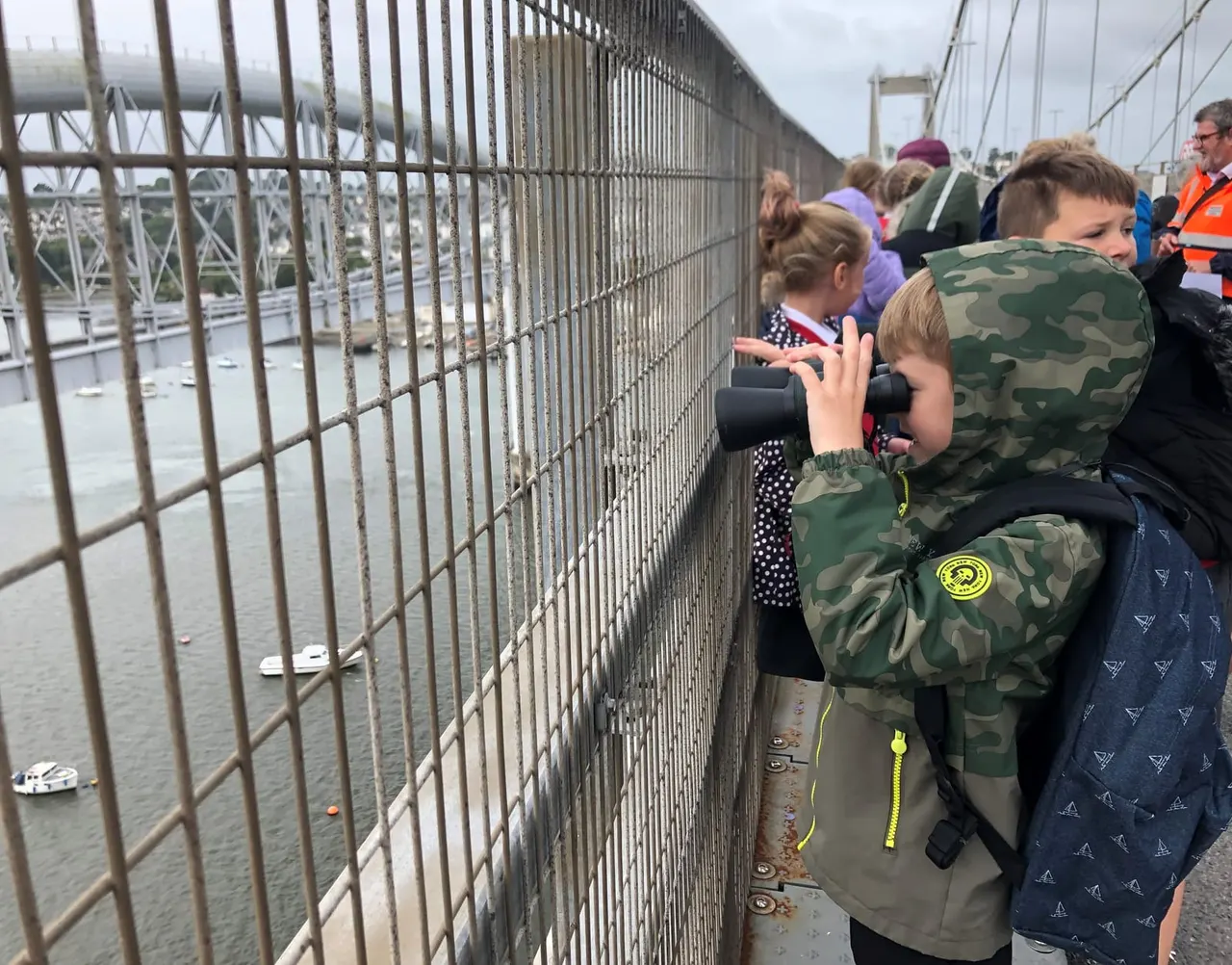 Children on a bridge viewing platform looking through binoculars at the river and landscape below.