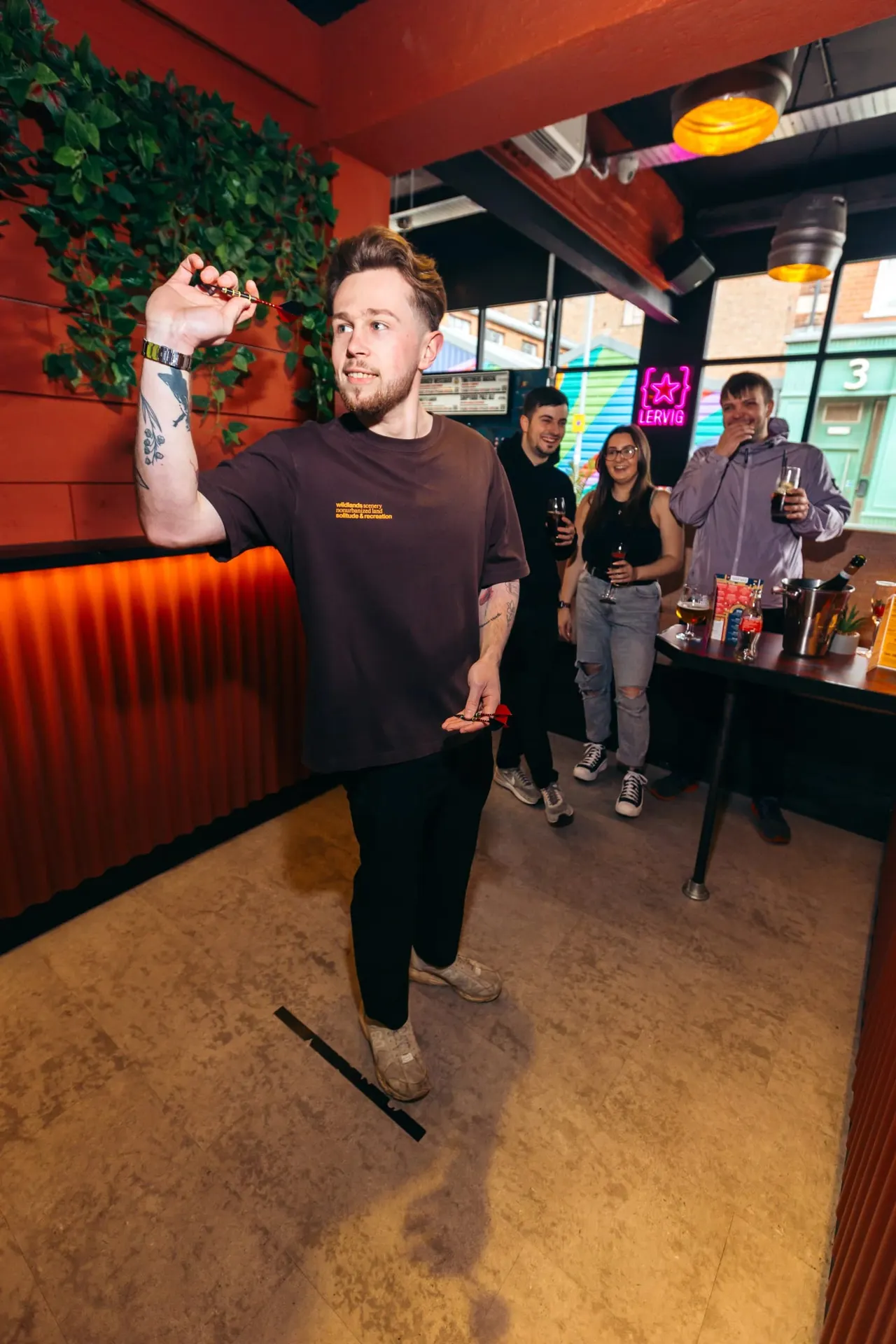 Man holding a medal aloft whilst celebrating with friends inside a vibrant red-walled bar with neon signage.
