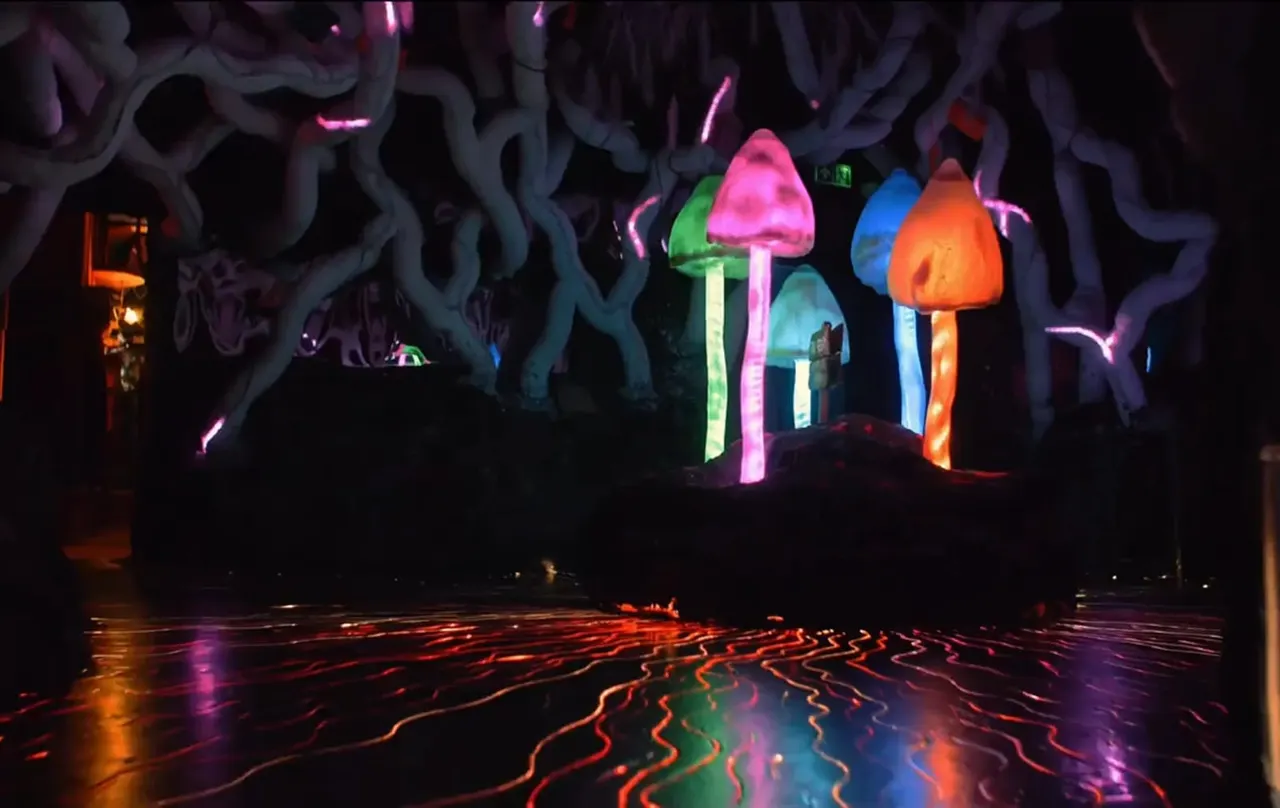 Neon-lit interactive installation featuring glowing mushrooms and serpentine vines in a dark indoor space with coloured floor patterns.