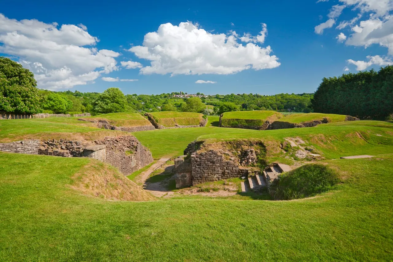 Ancient Roman stone ruins set into a green hillside beneath a blue sky with white clouds.