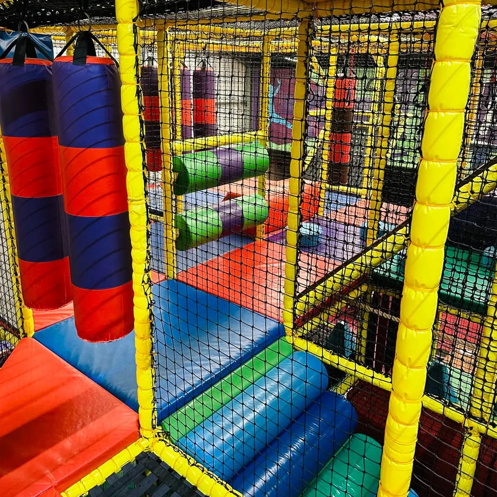 Colourful indoor play structure with netting, foam tunnels and padded surfaces in bright primary colours.