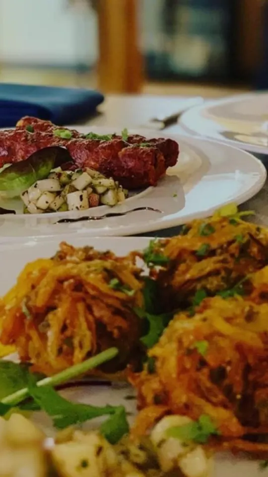 Close-up of plated curry dishes including spiced meat and potato items garnished with herbs and chutneys.