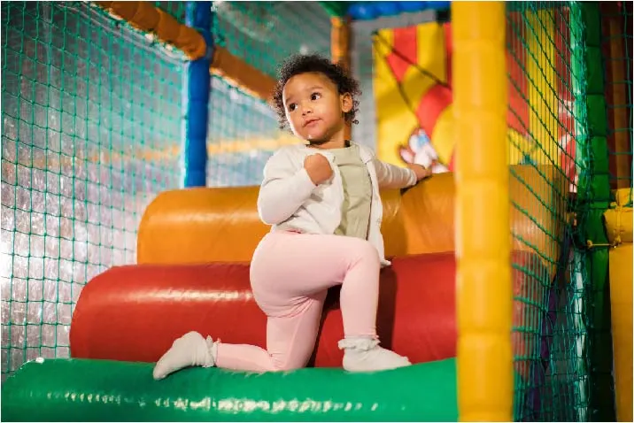 A toddler playing on colourful inflatable structures inside a soft play facility.