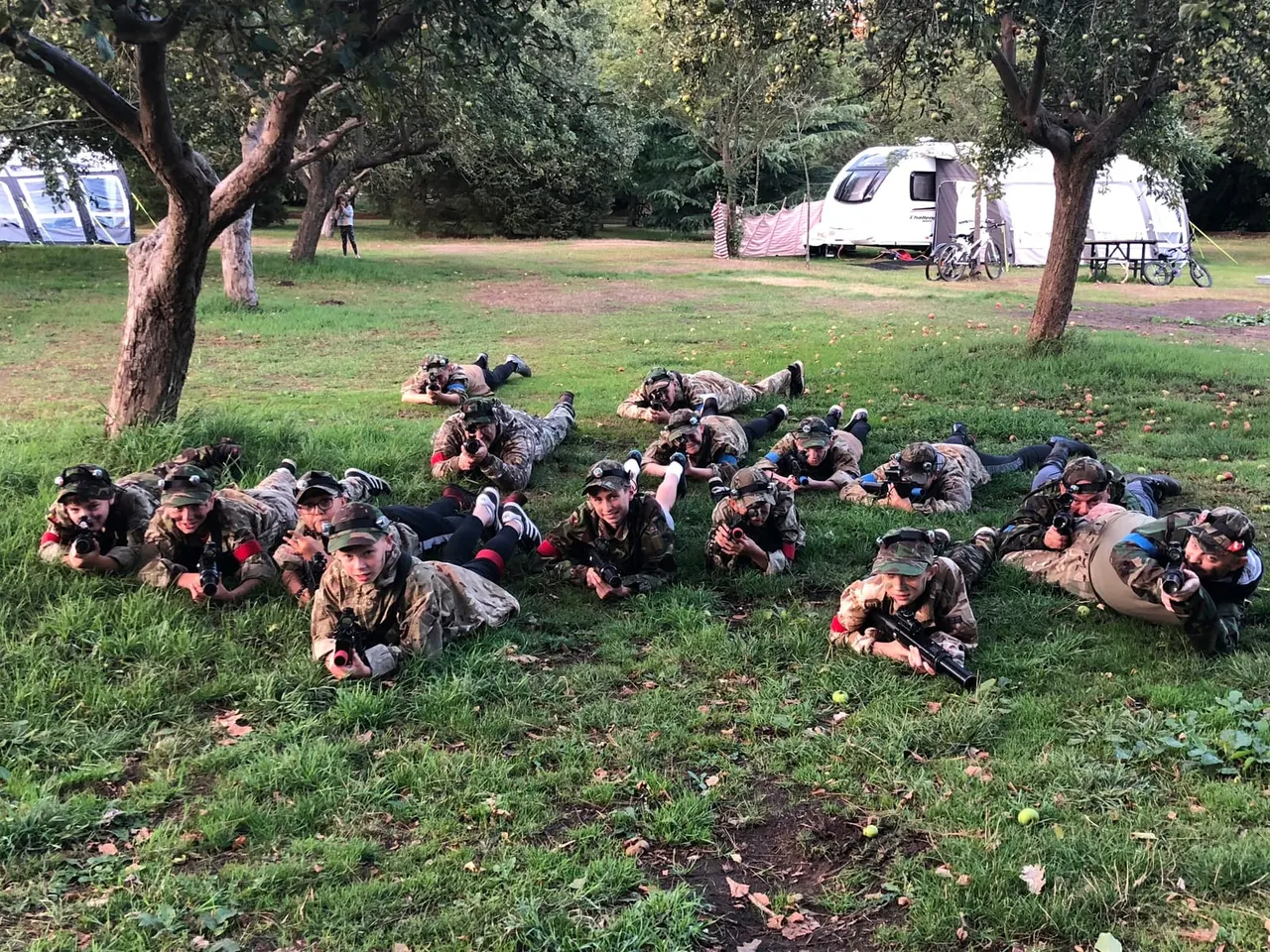 Children playing outdoor laser tag among trees with rifles raised