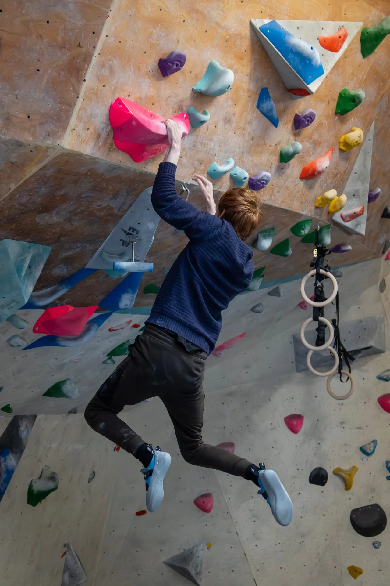 Person rock climbing on an indoor bouldering wall with colourful hand and foot holds.