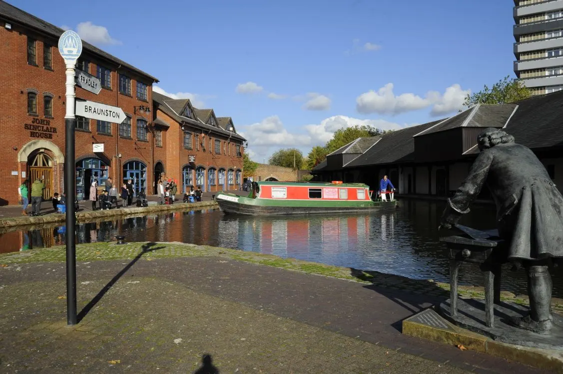 Historic brick buildings and a narrowboat moored on the canal at Coventry Canal Basin, with visitors on the towpath.