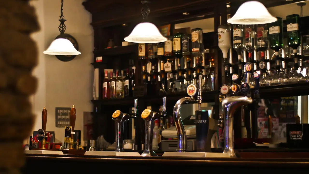 Bar counter with beer taps and pumps, shelves of bottles behind, and pendant lights overhead.