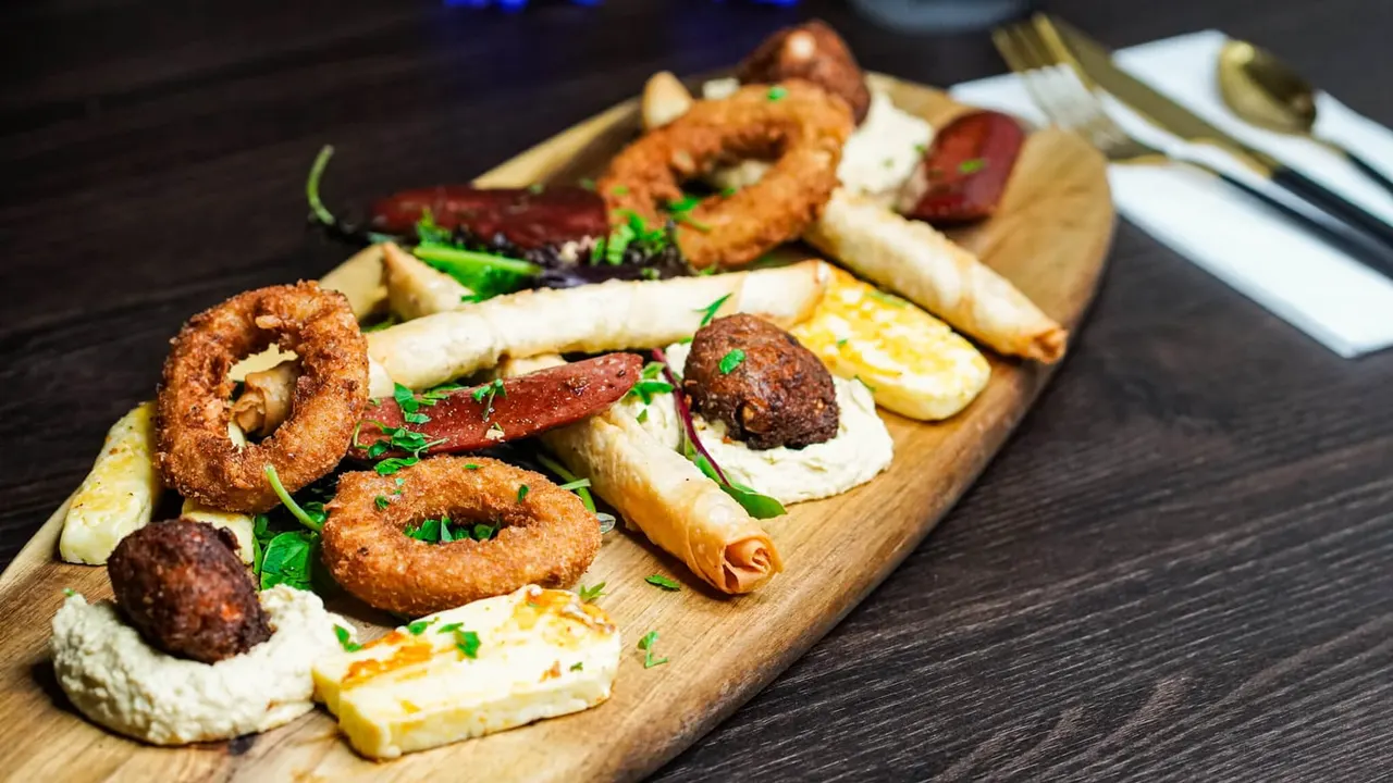 Sharing board with fried onion rings, meat kebabs, cheese, fresh vegetables and bread on wooden platters.