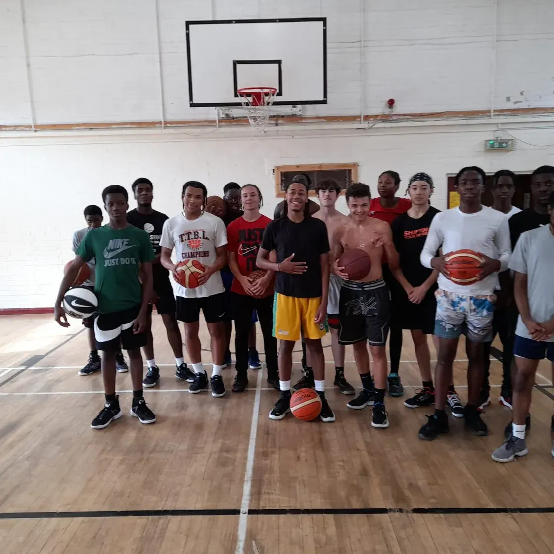 Group of young people posing together on a basketball court holding basketballs.