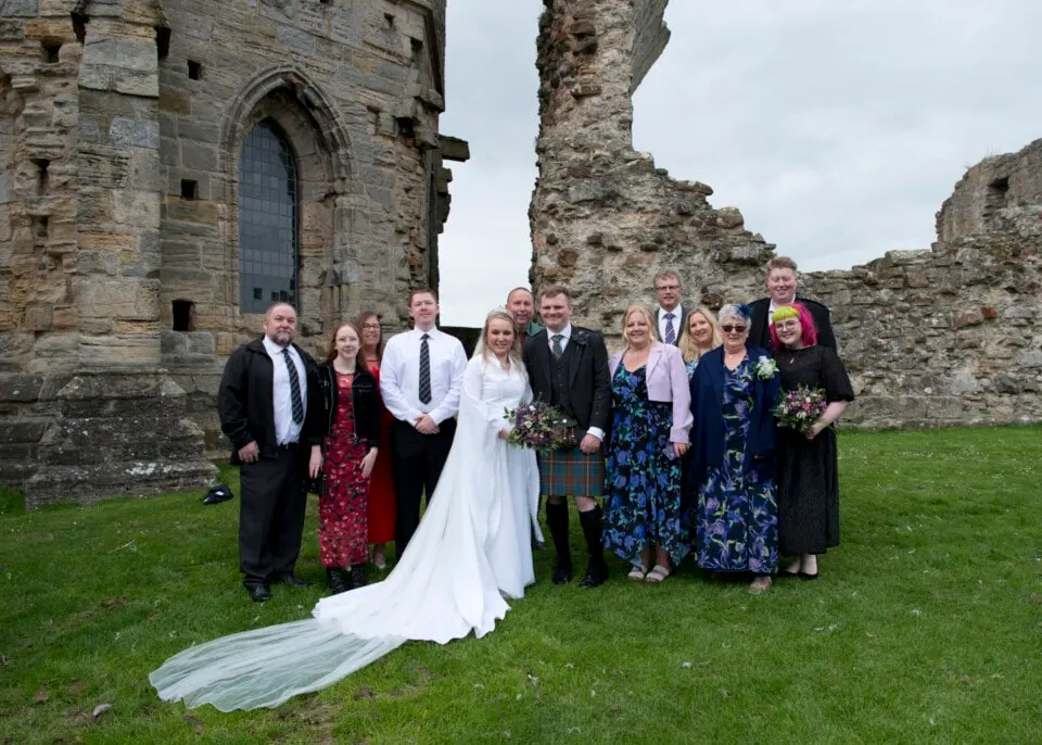 Wedding party posing with bride and groom in front of historic stone castle ruins.