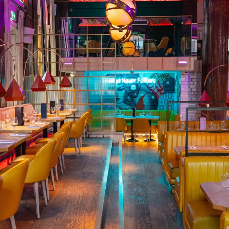 Vibrant modern restaurant interior with yellow chairs, colourful pendant lights, and illuminated turquoise feature wall.