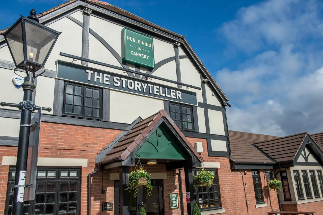 Traditional Tudor-style pub building with cream and dark timber framing, red brick lower section, and green entrance canopy under clear blue sky.