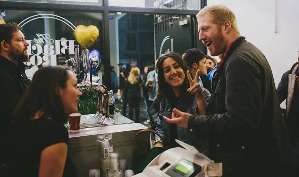 People smiling and chatting at a bar counter during an indoor event or gathering.