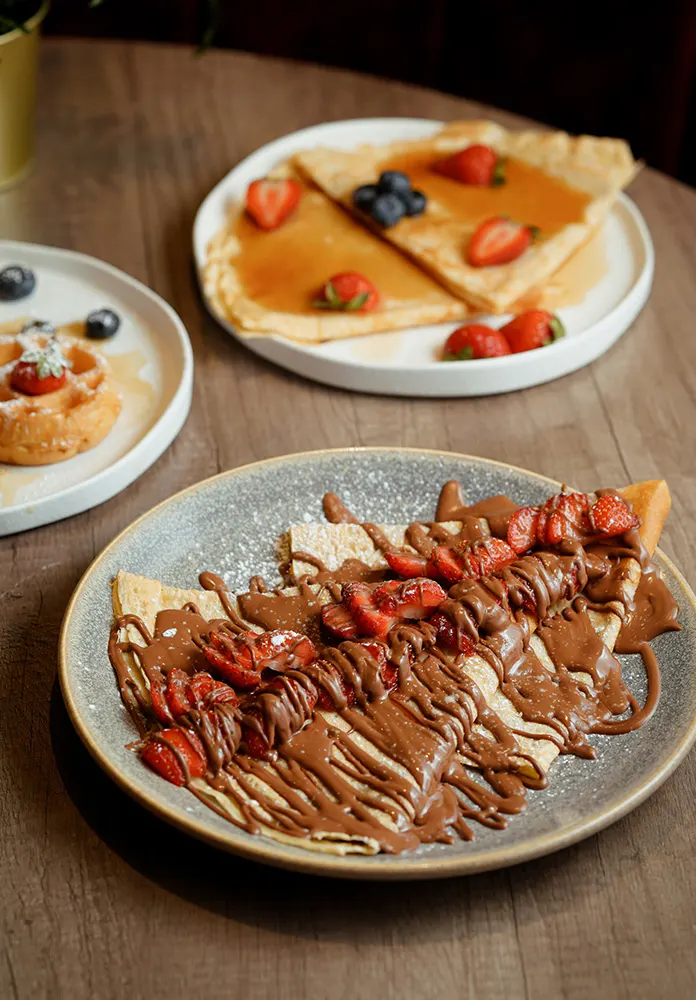 Crêpes with chocolate spread, strawberries and blueberries on wooden table.