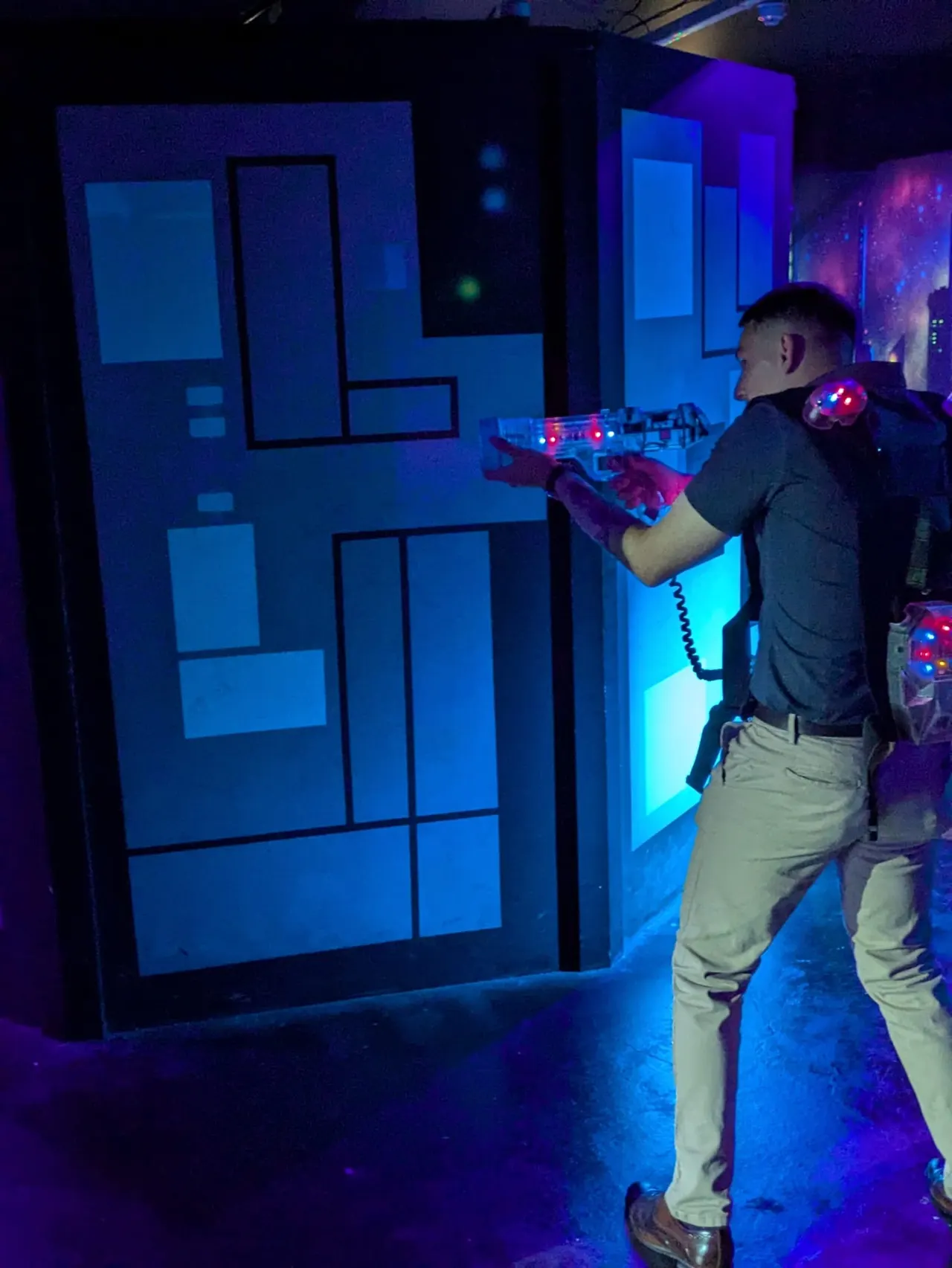 Man playing laser tag in a darkly lit arena with illuminated blue geometric walls.