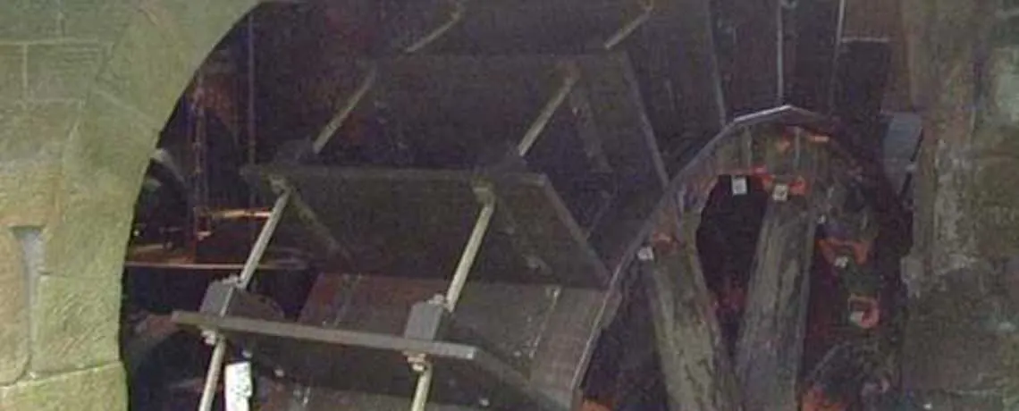 A large metal water wheel mechanism with geometric blade segments visible inside an industrial stone building.