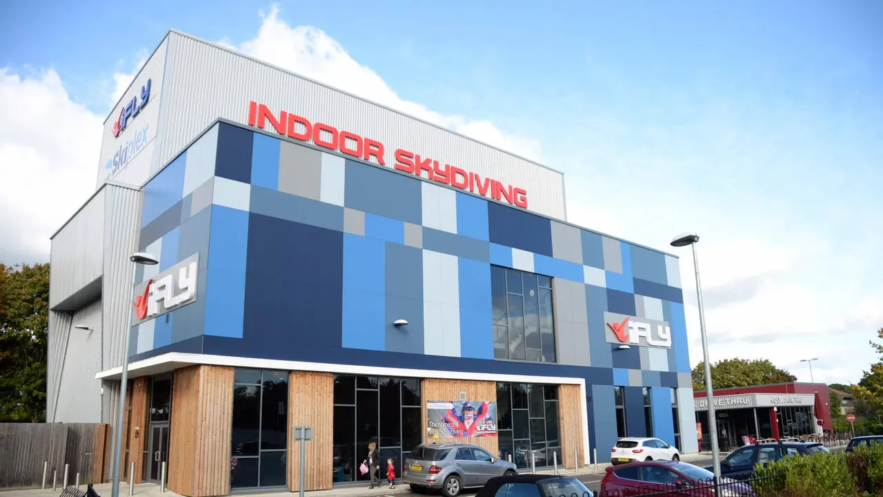 Modern indoor skydiving facility building with blue and white checkered exterior and wooden entrance doors.