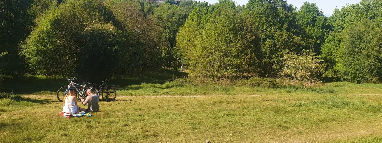Two cyclists rest on grass in a woodland clearing with their bikes propped behind them.