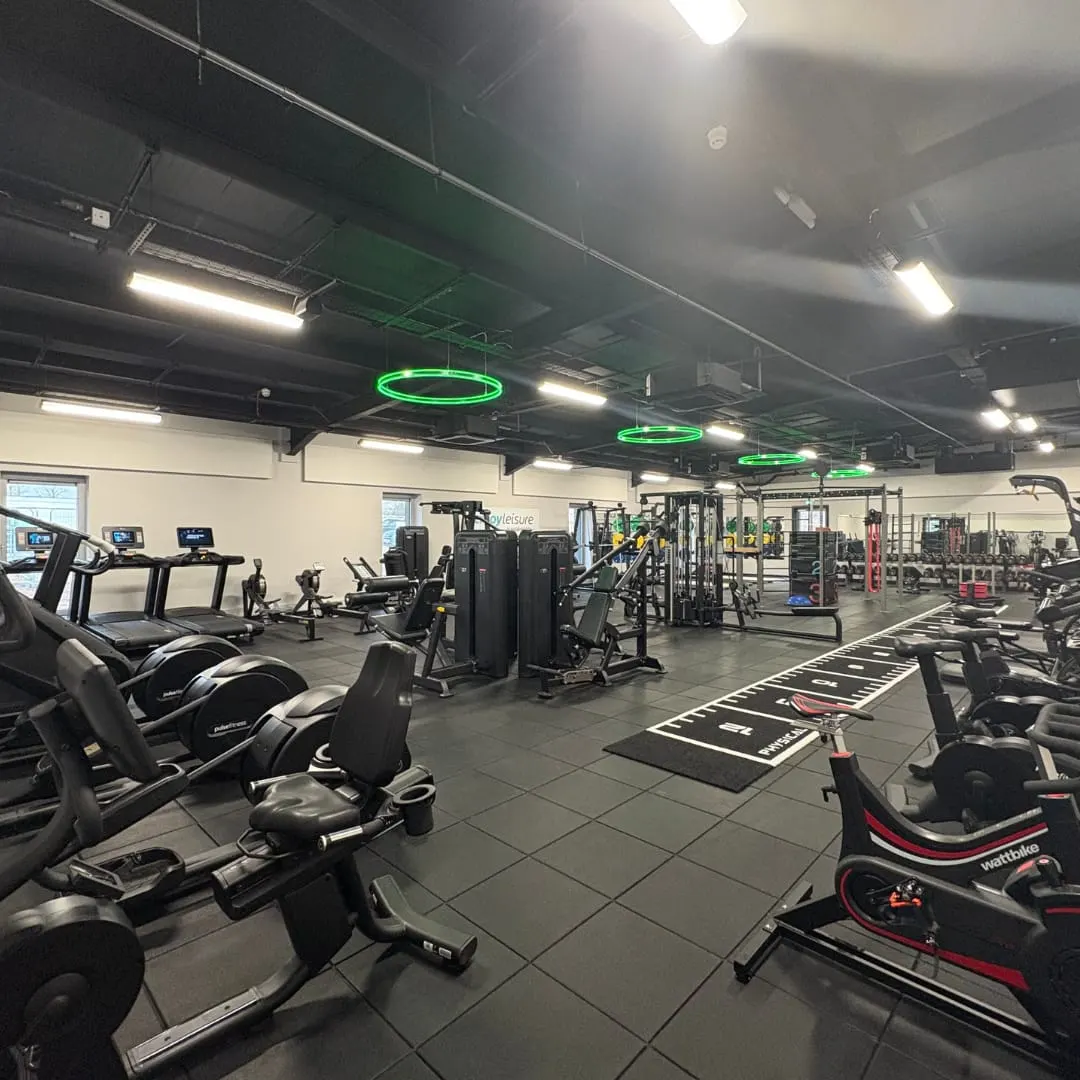 Modern gym interior with exercise bikes, treadmills, weight machines and green neon lighting overhead.