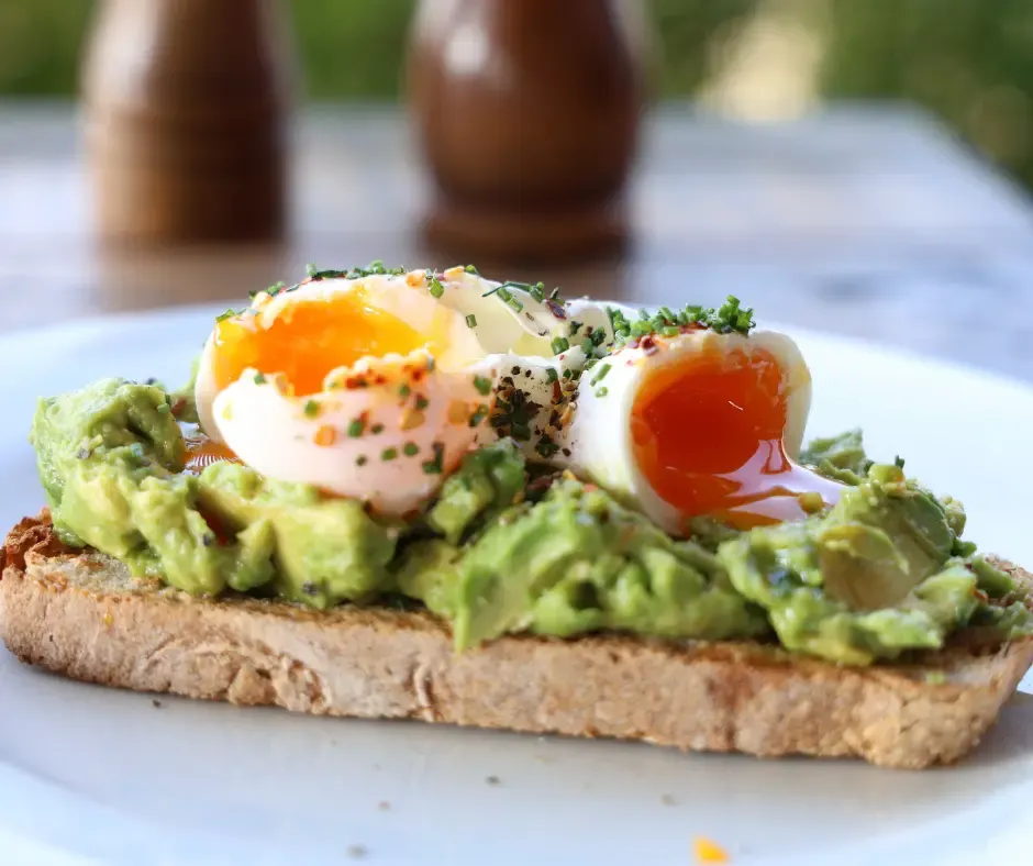 Toasted bread topped with avocado and two soft-boiled eggs with runny yolks, garnished with herbs and spices.