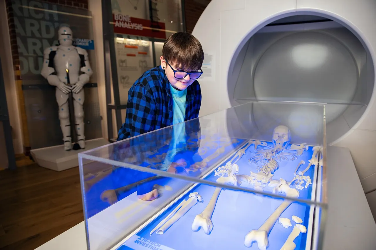 Child wearing blue checked shirt and purple glasses examining interactive display of skeletal remains in museum exhibit.
