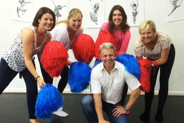 Five people posing together holding large red and blue pom-poms indoors.