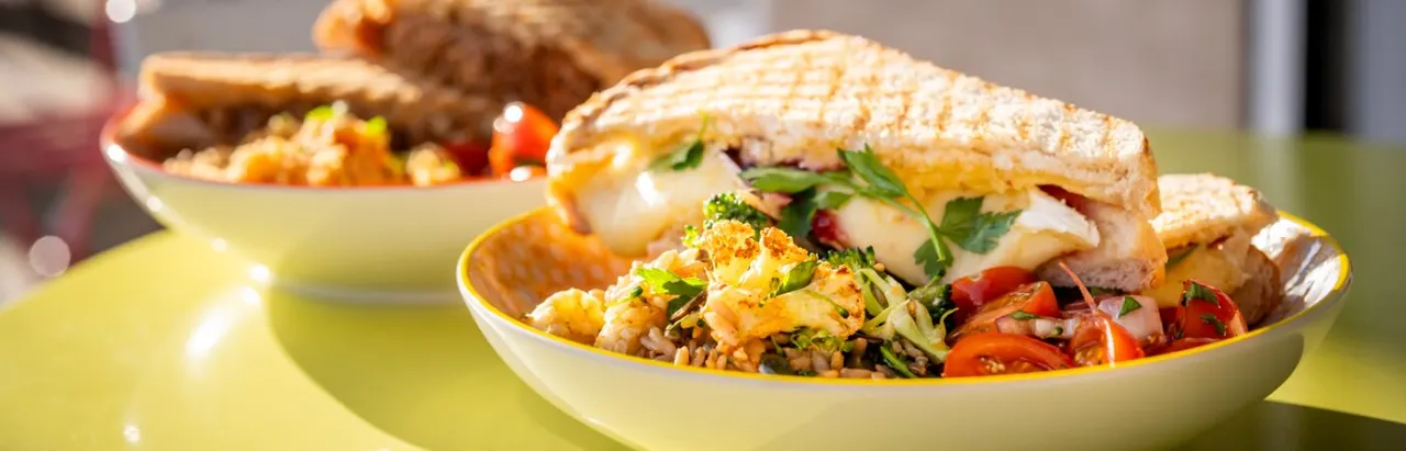 Crusty sandwich filled with seafood, salad and herbs, served in a bowl with mixed vegetables and garnish.