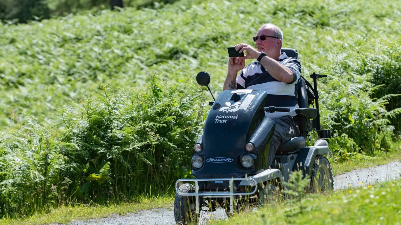 Man taking a photograph whilst riding a trike along a country path surrounded by green vegetation.