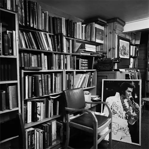 Person browsing books in a cramped black-and-white interior lined with shelves of used books and vintage furnishings.