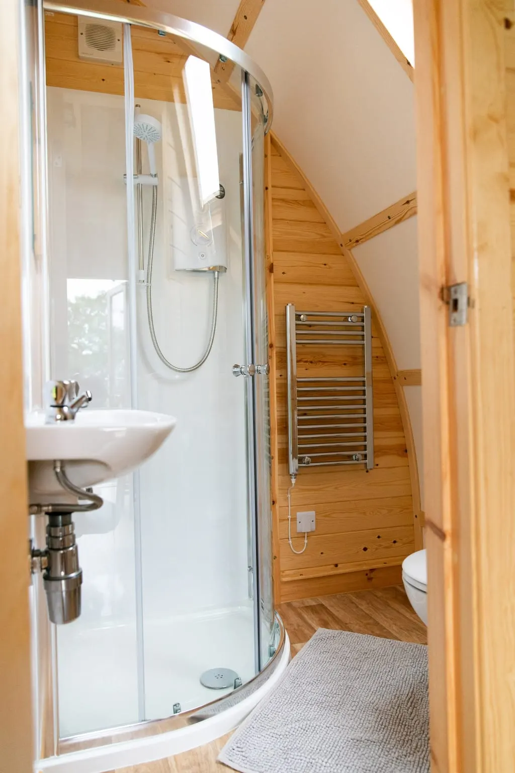 Modern bathroom with curved shower enclosure, white sink, heated towel rail and wooden beams in compact lodge interior.