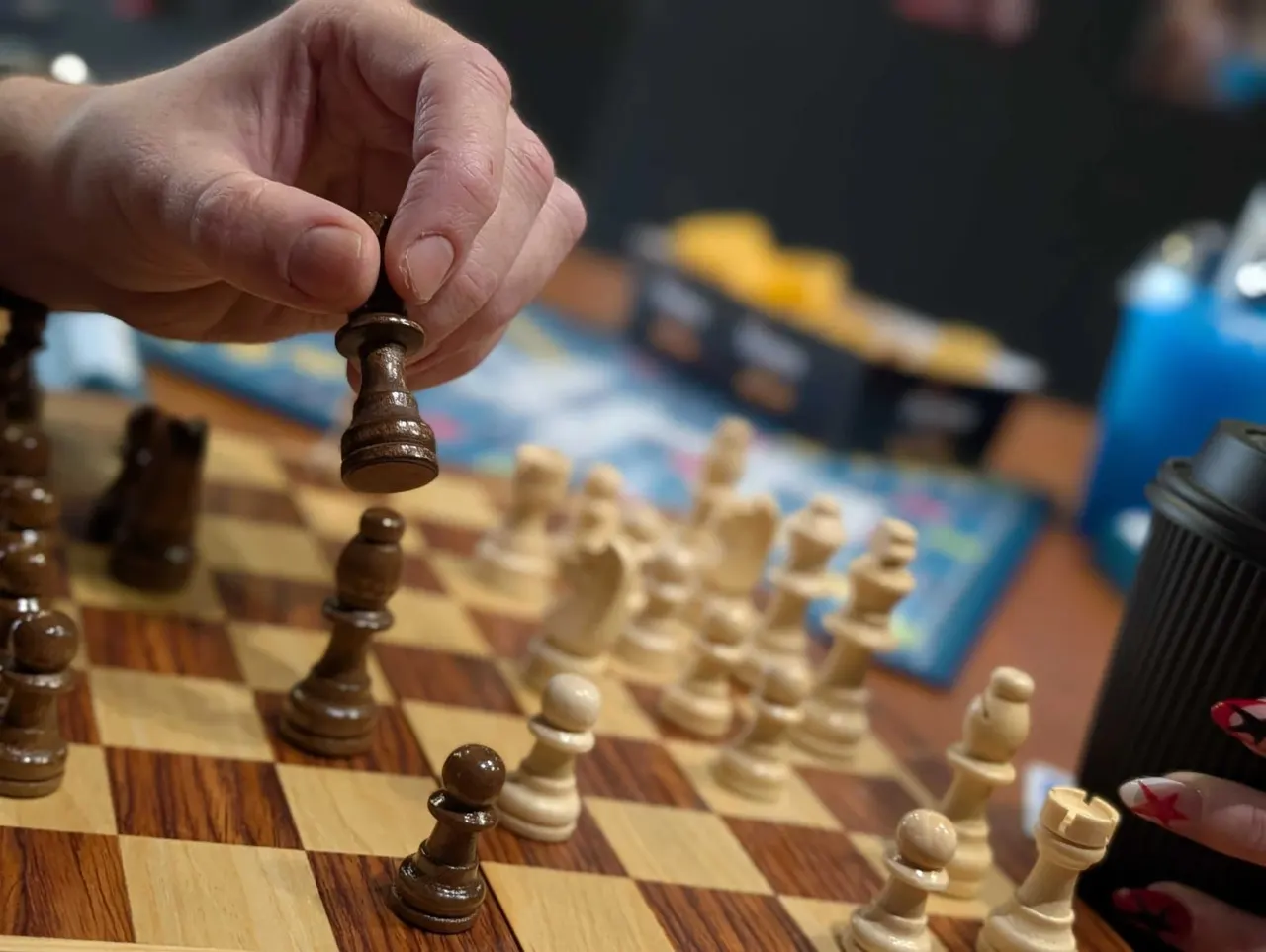 A hand moving a brown chess piece above a wooden chessboard during a game.