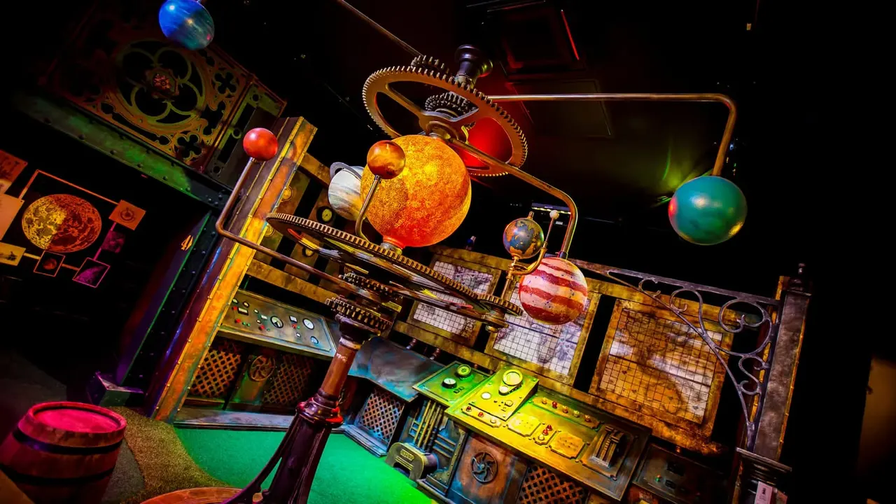 Illuminated indoor crazy golf course with a solar system theme, featuring glowing planet orbs and neon-lit obstacles against a dark background.