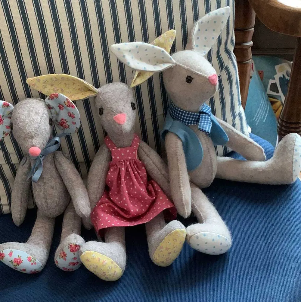 Handmade fabric rabbit soft toys dressed in colourful clothes, displayed on a striped chair.