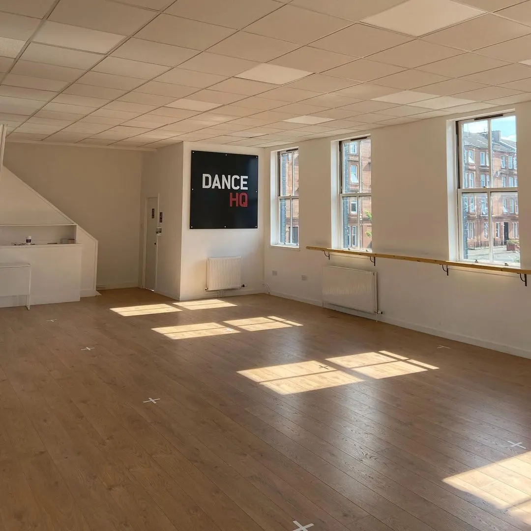 Empty dance studio with wooden floor, mirrored wall, barre, and 'Dance HQ' sign.