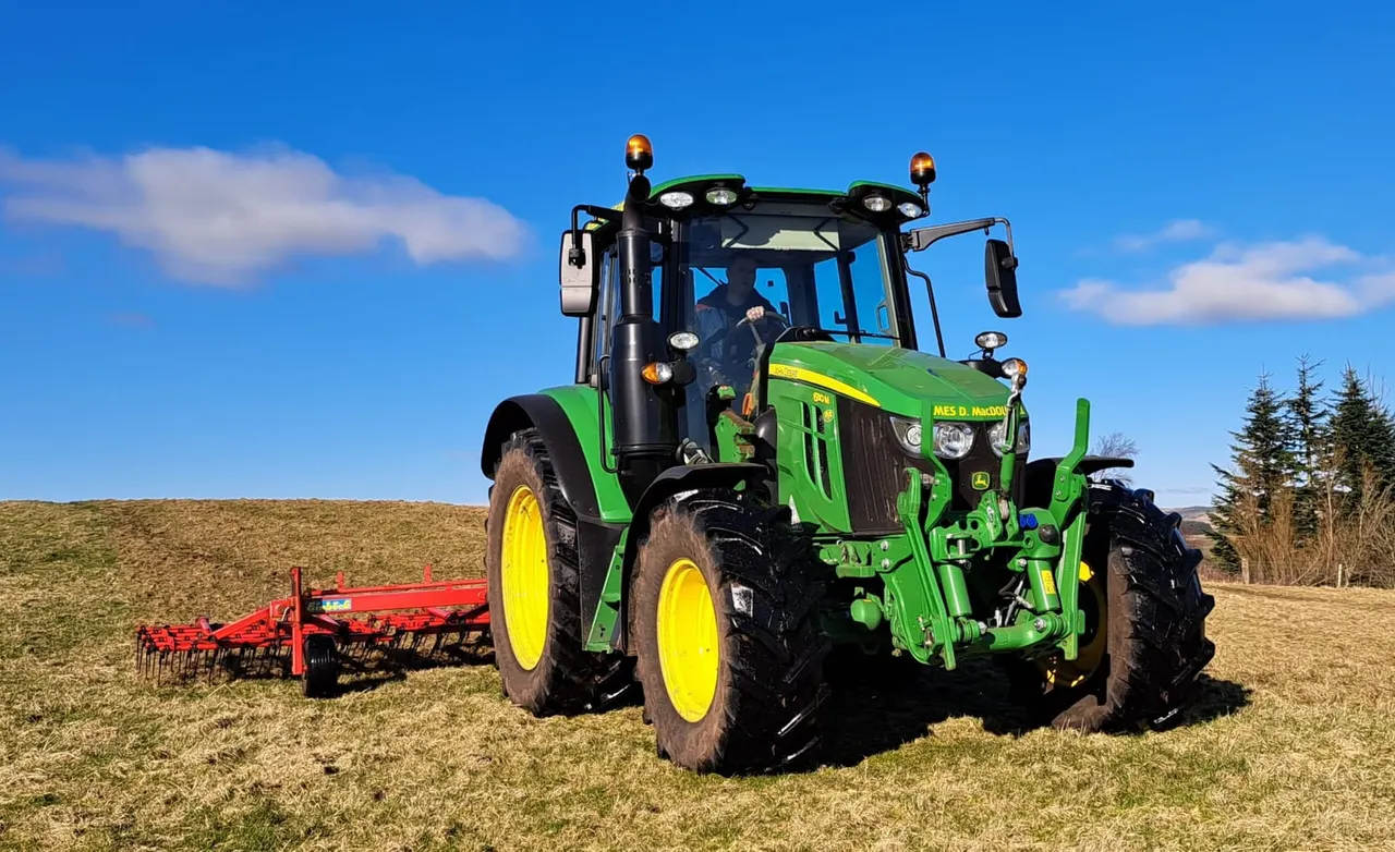 Bright green and yellow tractor with red ploughing equipment in a ploughed field under blue sky.