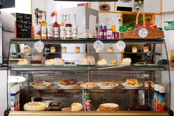 A multi-tiered display counter in a farm shop showing baked goods, pastries, and bottles of spirits for sale.
