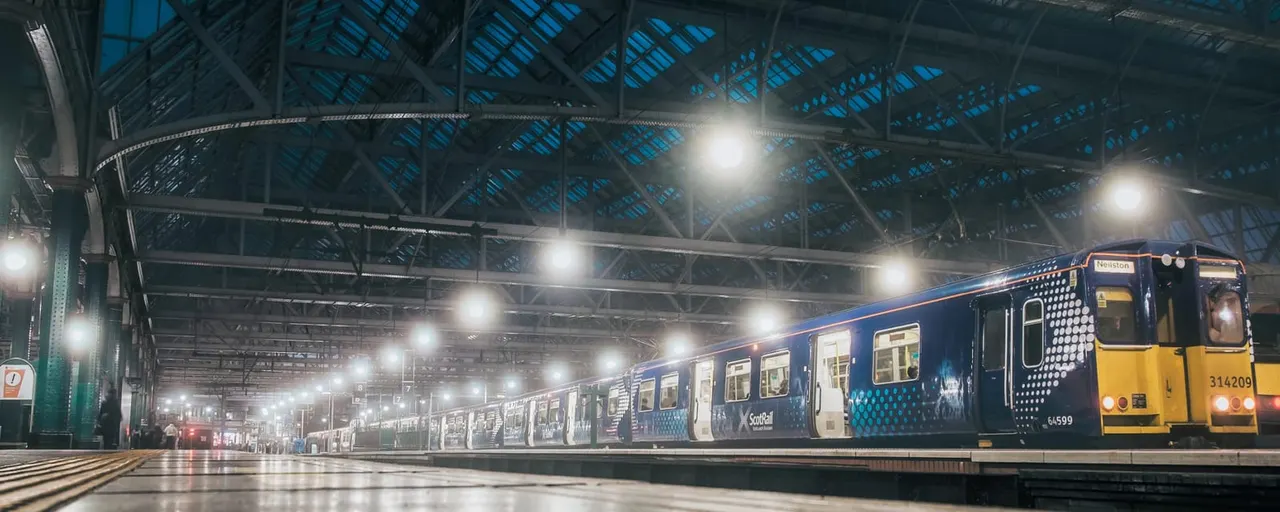 Blue and yellow passenger trains parked at an illuminated railway station platform under a Victorian iron roof.