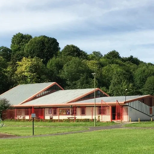 A red-roofed soft play building with cream-coloured walls set in a green field backed by trees.