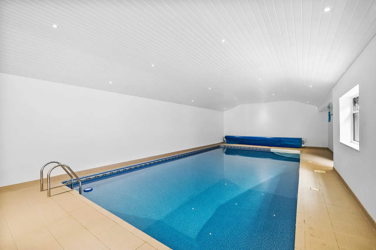 Indoor swimming pool with blue water, metal handrails, and a blue roller cover at the far end.
